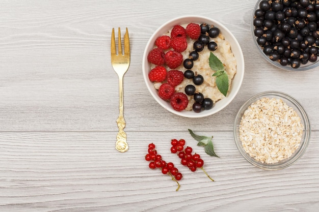 Oatmeal porridge in porcelain bowl with currant berries and raspberries decorated with mint leaves