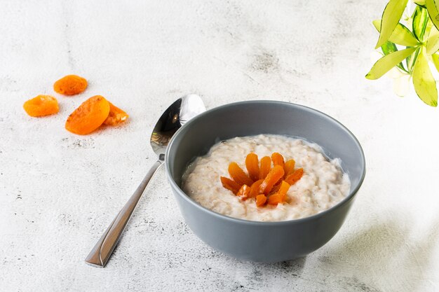 Porridge di farina d'avena o avena di porridge o cereali per la colazione con albicocche secche isolate su fondo di marmo bianco. cibo fatto in casa. gustosa colazione messa a fuoco selettiva. foto orizzontale.