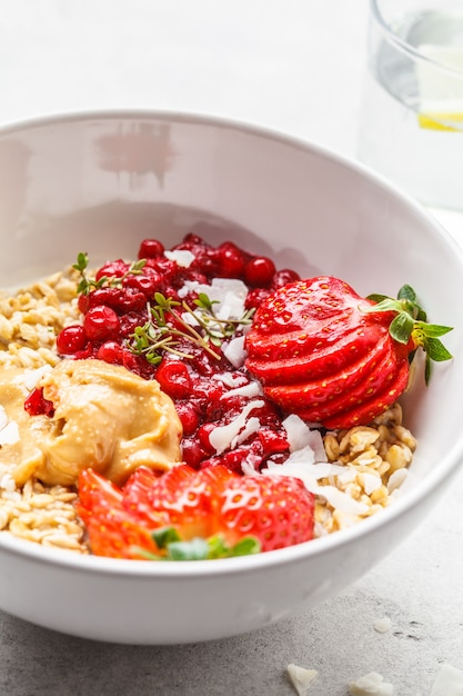 Oatmeal porridge with berries, peanut butter and coconut in white bowl. 