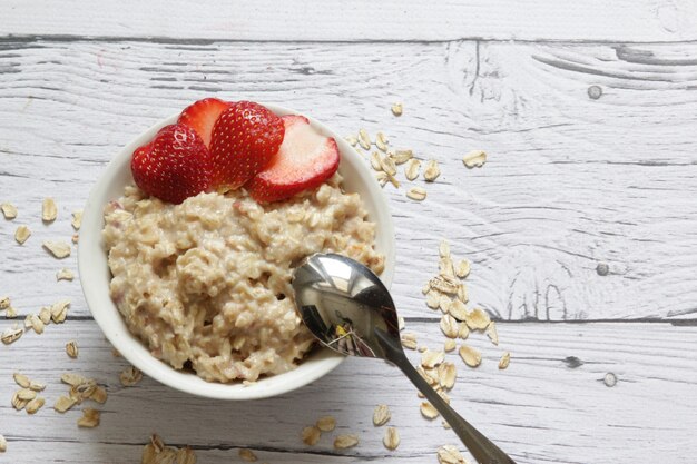 Oatmeal porridge with fresh strawberries on a wooden background. Red berries in the background.