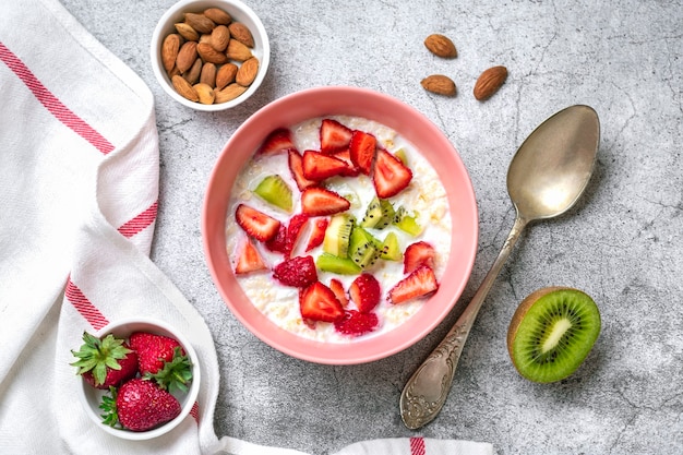 Oatmeal porridge with slices of kiwi strawberries almonds in pink bowl spoon napkin with red stripes...