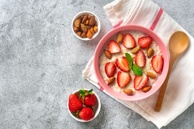 Oatmeal porridge with strawberries almonds mint leaf in pink bowl spoon and napkin with red stripes ...