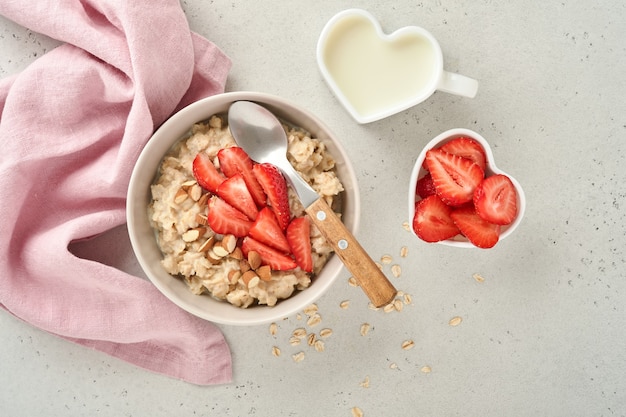 Oatmeal porridge with strawberry slices, nuts almonds and honey in blue bowl on grey table. Healthy eating, dieting, vegetarian food concept. Place for text