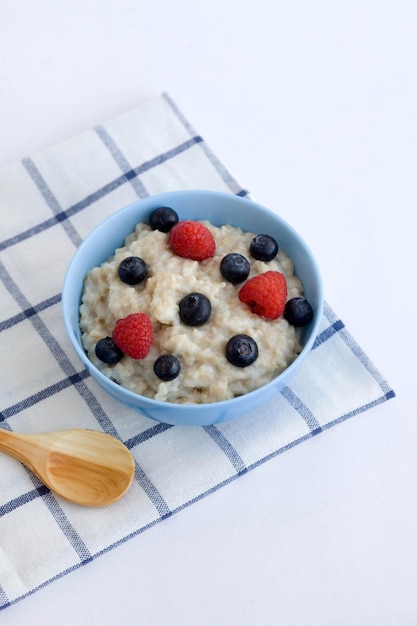 Oatmeal on water with berries in a blue plate on a white background Diet breakfast for weight loss