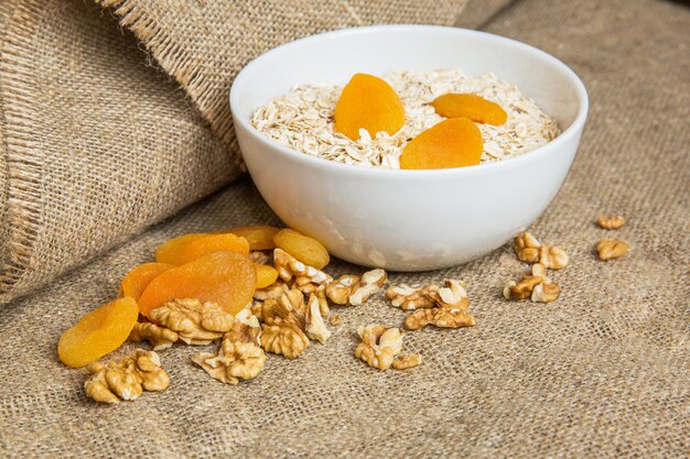 Oatmeal in white bowl with dried fruits and nuts on light brown textile background