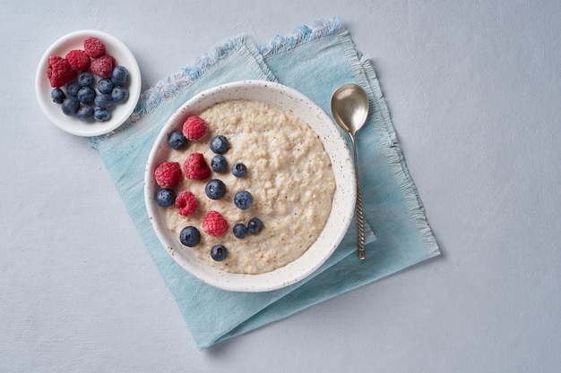 Oatmeal with blueberries, raspberries on blue light background. Top view. Healthy diet breakfast