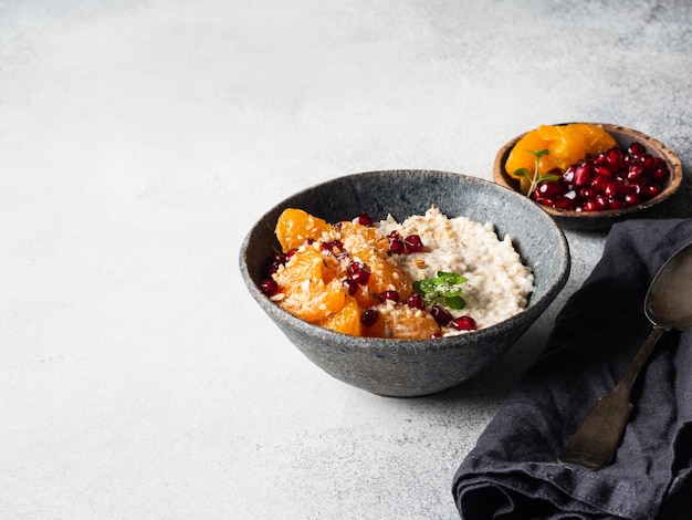 Oatmeal with fresh tangerine slices and pomegranate seeds, ground almonds and mint in a blue bowl on grey background. Copy space