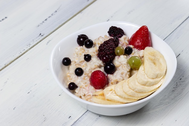 oatmeal with fruits in a white bowl on a white wooden table