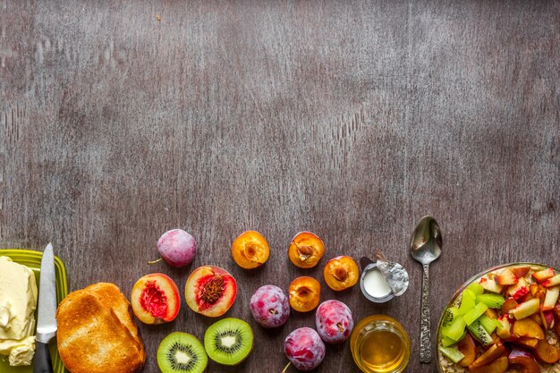 Oatmeal with plums, kiwi and peach, toast with butter and honey on a wooden table. A cup of black tea. The concept of a healthy breakfast. Top view. Copy space. Still life. Flat lay