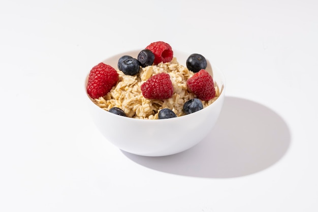 Oatmeal with raspberries and blueberries in white bowl on white table. Top view.