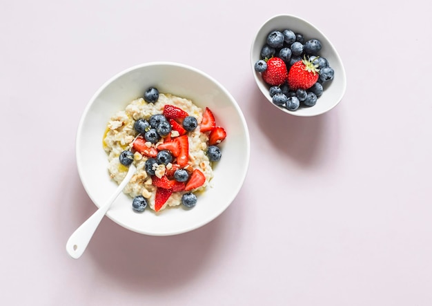 Oatmeal with strawberries blueberries nuts and honey on a light background top view