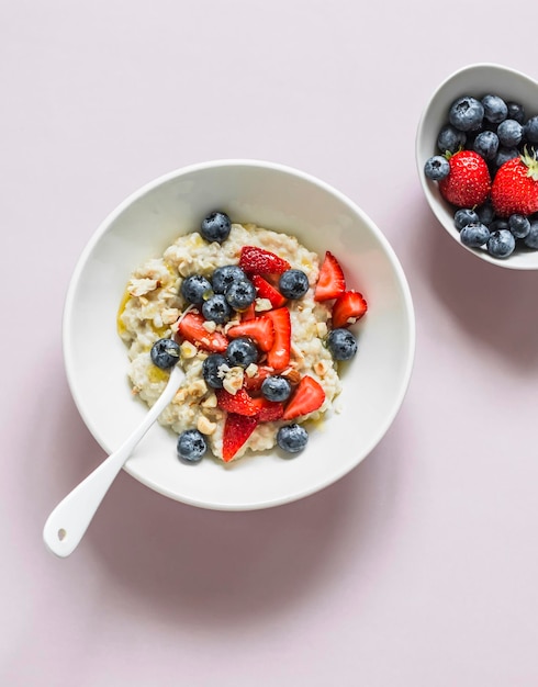 Oatmeal with strawberries blueberries nuts and honey on a light background top view