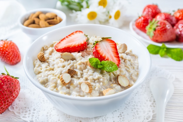 Oatmeal with strawberry and nuts in bowl on white wooden table.