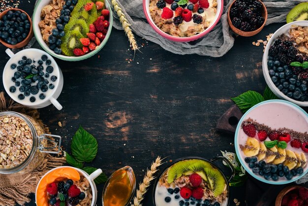 Farina d'avena con yogurt, frutta e bacche in piatti colazione su uno sfondo di legno nero vista dall'alto spazio libero per il testo