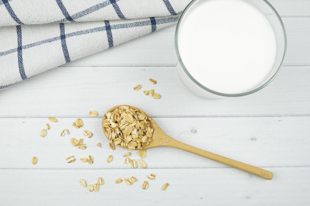 Photo oatmeal in a wooden spoon, a glass of milk and tea towel on light background. healthy breakfast concept, oat milk, food for allergy sufferers and vegetarians. top view