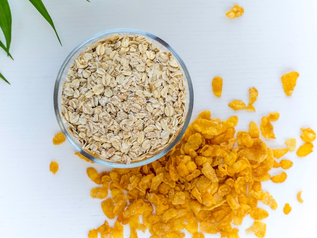 Oats in a bowl and cornflakes around isolated