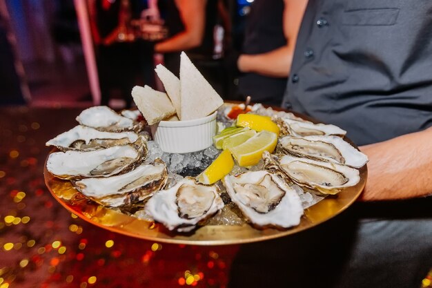 Ober houdt in handen dienblad met oesters en citroen op ijs Delicatesse zeevruchten