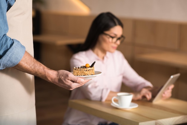 Ober serveert taart voor zakenvrouw met behulp van digitale tablet in café focus op voorgrond