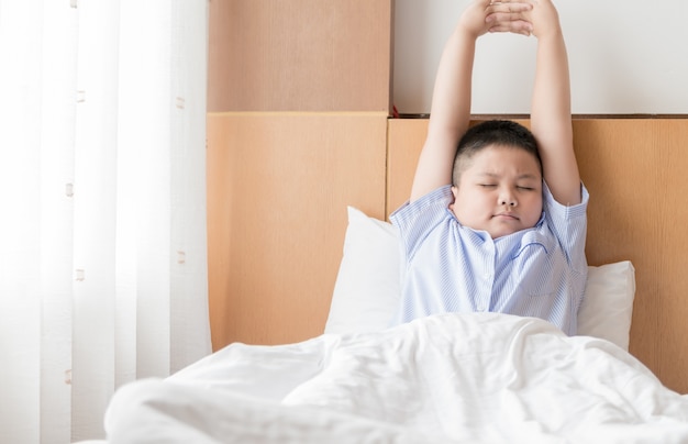 obese fat boy wakes up and stretching on bed in morning