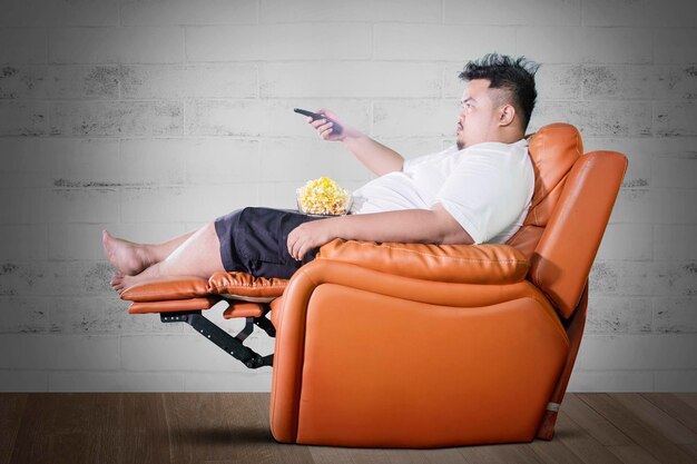 Photo obese man eats popcorn during watch tv at home