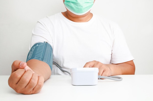 An obese man wearing a mask uses a blood pressure monitor on his arm himself obesity concept Risk of high blood pressure health care