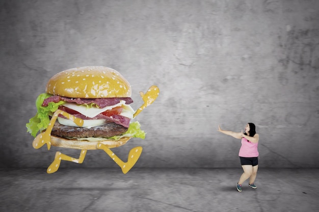 Photo obese woman running away from a hamburger