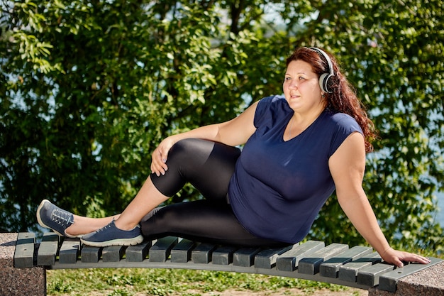 Obese woman with plus size body listens to music through wireless headphones