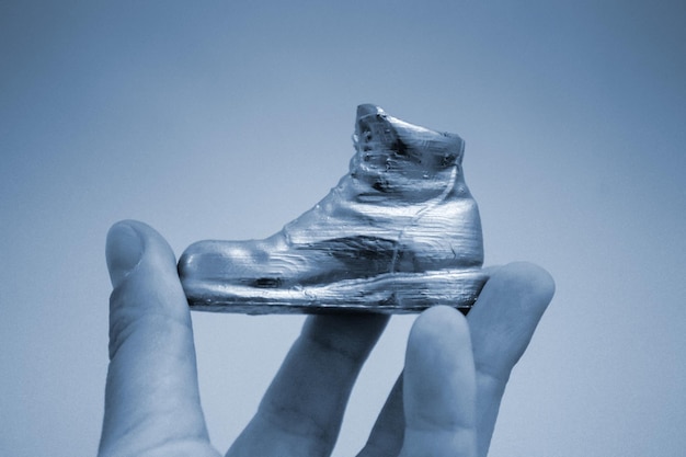 3Dプリンターで印刷され、手元にエナメルで覆われたブーツの形をしたオブジェクトクローズアッププログレッシブモダンアディティブテクノロジーブルーグレーカラーコピースパーゼ