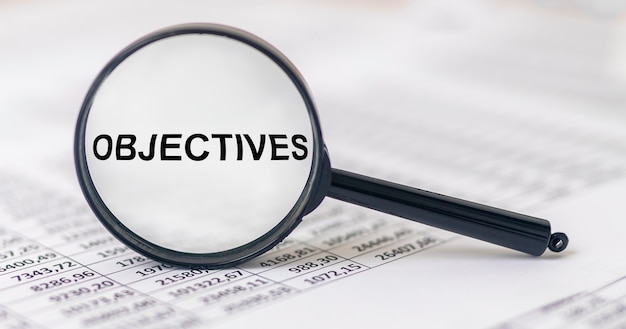 Objectives word inscription through magnifying glass on financial documentss, business goals.