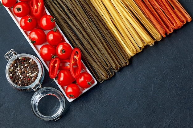 An oblong plate with tomatoes and paprika colorful noodles with natural vegetable ingredients and a glass jar of spices