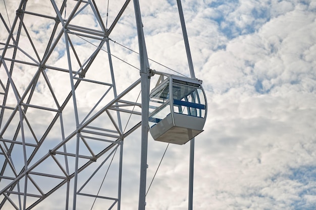 Observation wheel cabin close up, blue sky background. White passenger car of big Ferris wheel in amusement park, view from ground. Bird's Eye view attraction with panoramic observation