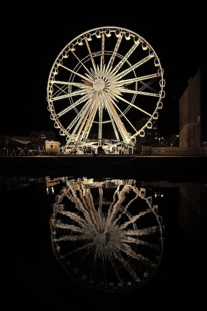 Observation wheel in Gdansk Poland at night Pleasure attraction with illumination and reflection in dark water Sightseeing and travelling Vacation and wanderlust