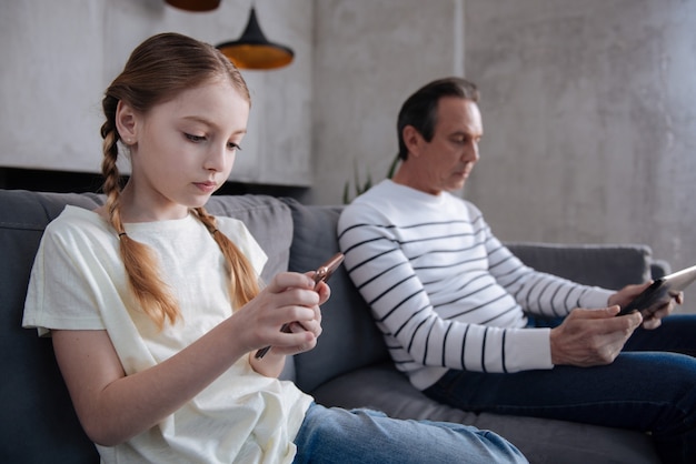 Obsessed skillful cute girl sitting at home and using digital gadgets with grandfather while surfing the Internet and playing games