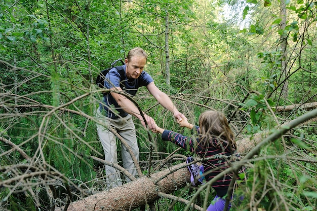 Obstakels overwinnen tijdens het wandelen in het bos. De volwassene helpt het meisje de omgevallen boom over te steken.