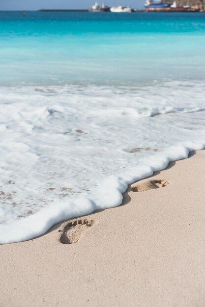 Oceaangolven raken de voetafdrukken op het tropische strand