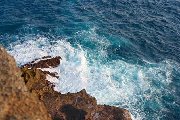 Океанская волна бьется о скалу при заходе солнца.