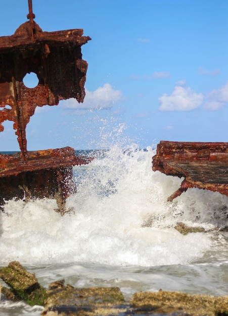 Ocean waves pound hard a rusted sunken ship stranded on the\
sand of australia