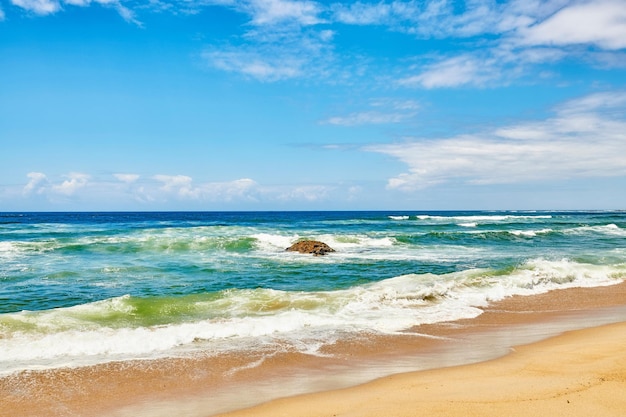 Ocean waves turbulent sea and rough tides from strong winds crashing onto a boulder at the beach shore with a cloudy blue sky copy space background Rocky seaside view landscape and coastal scenery