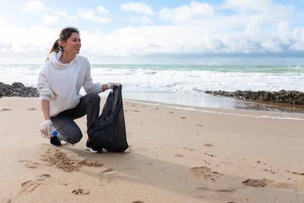 Ocean39s pollutions Young female volunteer putting plastic bottles in bag cleaning coastal zone panorama free space