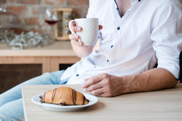 Ochtend gezelligheid Thuis eenzaamheid Ontbijt tijd Man met kop warme drank en croissant Keuken ruimte