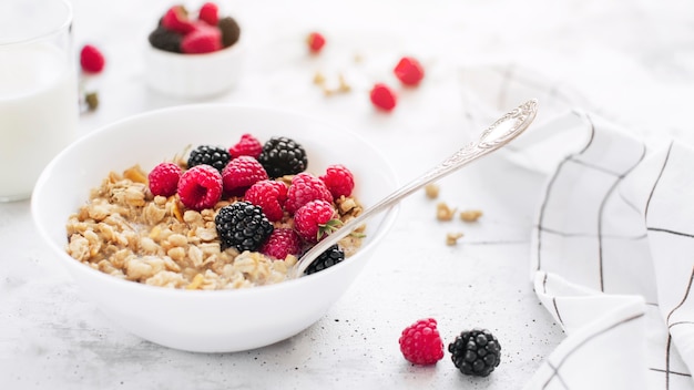 Ochtend gezond ontbijt, witte kom vol met muesli, muesli, framboos, braam op grijze betonnen tafel. Gezond eten, eco, bio food concept. Verse smakelijke maaltijd op grijze achtergrond. Kwaliteitsfoto