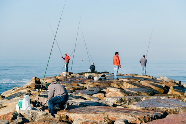 Ochtend in de atlantische oceaan in portugal. groep onherkenbare volwassen mannen vissen. onbekende visser met hengel. visspullen. rotsachtige pier.
