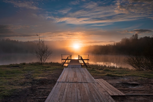 Ochtend over een mistig meer met een houten pier in het bos in de vroege ochtend