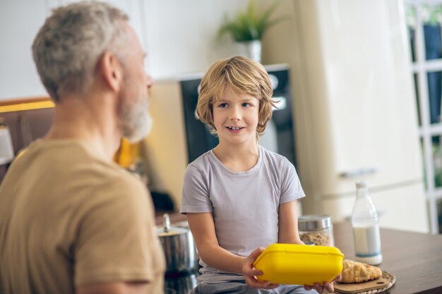 Ochtend thuis. Grijsharige man in beige t-shirt en zijn zoon in de keuken thuis