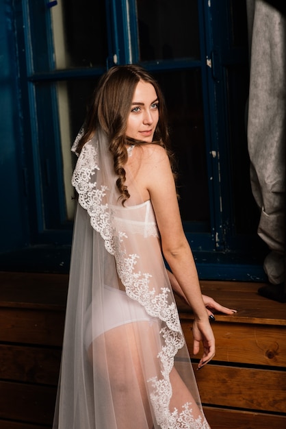Ochtend van de bruid. Portret van een mooie jonge vrouw in een wit ondergoed en een peignoir.