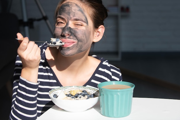 Ochtendontbijt gezichtsbehandeling mooie jonge vrouw met houtskool modder gezichtsmasker op de gezichtshuid