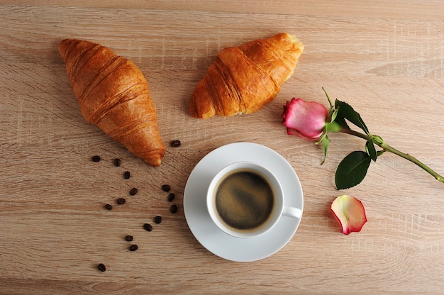 Ochtendontbijt - twee croissants, koffie en rode roos met gescheurde bloemblaadjes