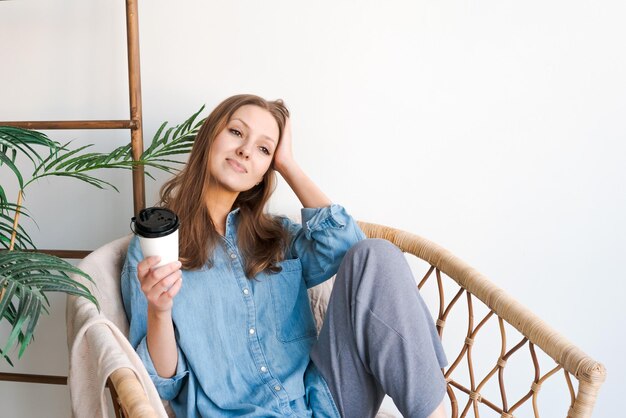 Ochtendontspanning Meisje zit in een rieten stoel en geniet van koffie in een gezellig huis