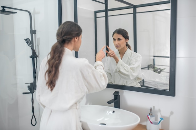 Ochtendprocedures. Een foto van een jonge vrouw in een badjas in de badkamer