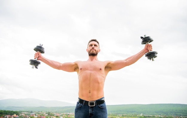 Ochtendtraining fitness en sportuitrusting succes Perfecte biceps atletisch lichaam Halter sportschool man sportman Gewichtheffen Gespierde man oefenen in de ochtend met barbell voel de vrijheid